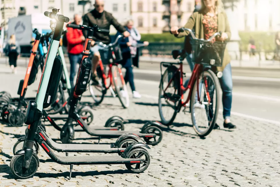 Parked electric scooters on a sidewalk with person walking bike in the background